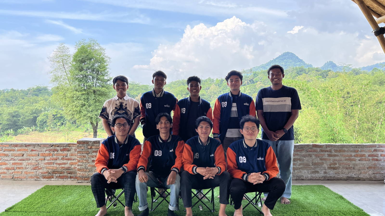 Sembilan pemuda berjaket almamater berfoto bersama di saung bambu kawasan dengan latar bukit hijau